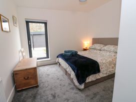 A bedroom with a bed covered with patterned bedding and a dark throw a wooden chest and a chair near a tall window at Dundarach in Aberfeldy