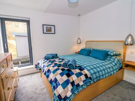 A bedroom with a wooden bed, blue plaid bedding, blue pillows, two rolled blue towels, wooden chest of drawers, pendant lights, and a window at Dundarach in Aberfeldy