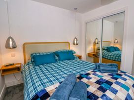 A bedroom with a bed covered in blue checkered bedding with two pillows and folded towels on top beside mirrored sliding closet doors and hanging pendant lamps at Dundarach Aberfeldy