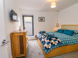A bedroom with a bed covered with checkered blue bedding and a wooden dresser near a window at Dundarach in Aberfeldy