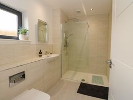 A bathroom with a glass shower, sink, toilet, small window with plant and mirror at Dundarach in Aberfeldy