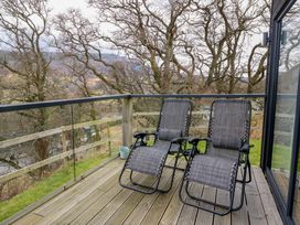 Two reclining chairs on a wooden deck with glass and wooden railing overlooking a wooded area at Dundarach in Aberfeldy
