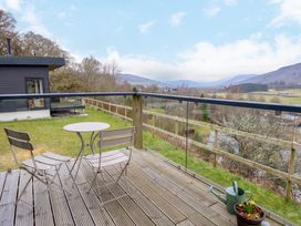 A balcony with two chairs and a table overlooking a grassy yard and distant hills at Dundarach in Aberfeldy