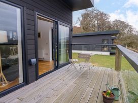 A wooden deck with metal table and chairs a potted plant and watering can outside a dark grey house at Dundarach in Aberfeldy
