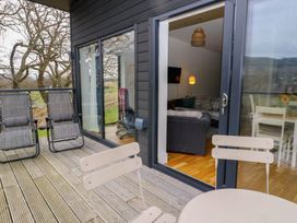 A balcony with chairs overlooking trees and a living room with a sofa and lamp at Dundarach in Aberfeldy