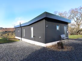 Exterior of a single-story dark gray building with windows and a bench on gravel at Dundarach in Aberfeldy