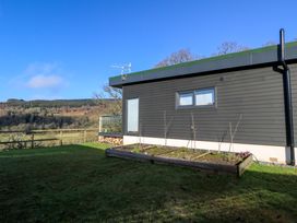 A backyard with a raised garden bed next to a dark gray building and a wooden fence overlooking trees and hills at Dundarach in Aberfeldy