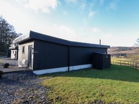 A modern single-story black wooden building with a gravel path and green lawn in a rural area at Dundarach in Aberfeldy
