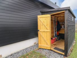 An open wooden shed with tools and gardening supplies next to a building with black siding at Dundarach in Aberfeldy