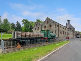 A green train engine with barrels on flatbed cars outside a stone distillery building at Dundarach in Aberfeldy