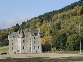 A stone castle with turrets near a forest and an open field at Dundarach in Aberfeldy