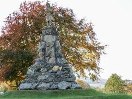 A stone statue monument with a figure on top and a relief sculpture below surrounded by trees with autumn leaves at Dundarach in Aberfeldy