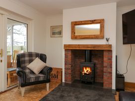 A lounge with a chair beside a glass door a brick fireplace with a wood-burning stove and a wooden framed mirror above at 14 Birchwood Road in Woolaston