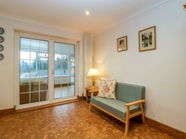 A sitting area with a small sofa a floral cushion a wooden side table with a lamp and glass doors leading to a sunroom at 14 Birchwood Road in Woolaston