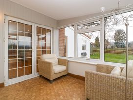 A sunroom with wicker armchairs and large windows showing a garden at 14 Birchwood Road in Woolaston