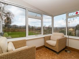 A sunroom with two wicker armchairs and a floor lamp with large windows overlooking a garden at 14 Birchwood Road in Woolaston