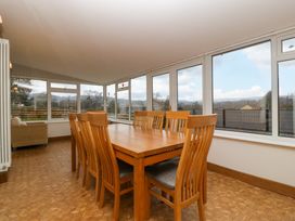 A dining room with a wooden table and eight chairs next to large windows overlooking a landscape at 14 Birchwood Road in Woolaston