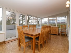 A dining room with a wooden table and chairs surrounded by large windows at 14 Birchwood Road in Woolaston
