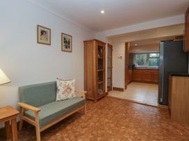 A small sitting area with a green sofa and a floral cushion a wooden display cabinet and a kitchen in the background at 14 Birchwood Road in Woolaston