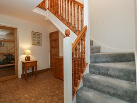 A hallway with a carpeted staircase wooden banister wooden doors a small wooden table with a lamp and a wooden cabinet at 14 Birchwood Road Woolaston