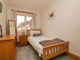 A small bedroom with a single bed a wooden dresser a nightstand with a lamp and a standing mirror at 14 Birchwood Road in Woolaston