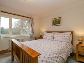 A bedroom with a wooden double bed and floral bedding two bedside tables with lamps and a window showing trees outside at 14 Birchwood Road in Woolaston