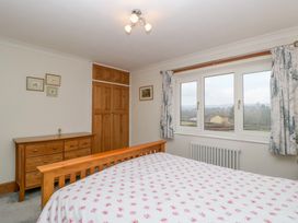 A bedroom with a wooden bed and dresser a window with curtains and a built in wooden wardrobe at 14 Birchwood Road in Woolaston