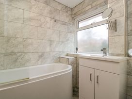 A bathroom with a bathtub a sink cabinet a frosted window and a wall-mounted mirror at 14 Birchwood Road in Woolaston