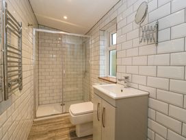 A bathroom with a shower enclosure, toilet, sink cabinet, wall-mounted mirror, and towel rail at 14 Birchwood Road in Woolaston