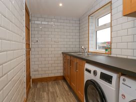 A utility room with wooden cabinets a washing machine a sink and a window at 14 Birchwood Road in Woolaston