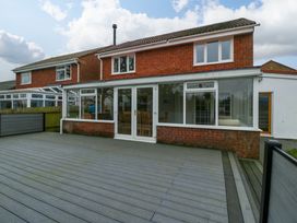 A backyard view of a two-story brick house with a large wooden deck and glass patio doors at 14 Birchwood Road in Woolaston