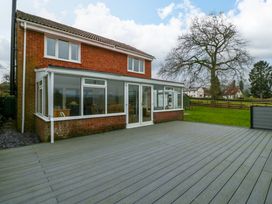 A two-story brick house with a large glass conservatory and a wide wooden deck in the backyard at 14 Birchwood Road in Woolaston