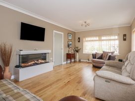 A living room with sofas a fireplace a wall mounted television and a window with vertical blinds at Bryn-Y-Glyn in Penrhyn Bay