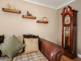 A living room with a leather armchair plaid cushions wooden shelves and a grandfather clock at Bryn-Y-Glyn in Penrhyn Bay