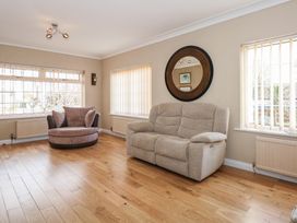 A living room with a beige sofa a round chair wooden floor and three windows at Bryn-Y-Glyn in Penrhyn Bay