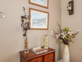 A wooden cabinet with a chess set a glass vase with flowers and a bottle next to a tall vase with flowers in a corner with framed pictures on the wall at Bryn-Y-Glyn in Penrhyn Bay