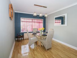 A dining room with a round glass table set with plates and glasses and four chairs at Bryn-Y-Glyn in Penrhyn Bay