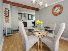 A dining area with a glass table and four chairs with a kitchen visible in the background at Bryn-Y-Glyn Penrhyn Bay
