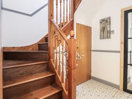 An interior view of a staircase with wooden steps and railing in a hallway with a patterned tile floor and a wooden door at Bryn-Y-Glyn in Penrhyn Bay