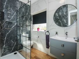 A bathroom with a shower area with black marble walls a toilet a sink with a cabinet a round mirror and a window with a black blind at Bryn-Y-Glyn in Penrhyn Bay