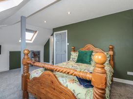 A bedroom with a carved wooden bed floral bedding green cushion gray carpet and a small bookshelf at Bryn-Y-Glyn in Penrhyn Bay