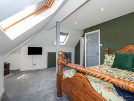 A bedroom with a wooden bed floral bedding skylight windows a TV on the wall a bookshelf and a gray door at Bryn-Y-Glyn in Penrhyn Bay