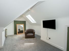 An attic room with a brown armchair mirror on the floor skylight window and a wall-mounted TV at Bryn-Y-Glyn in Penrhyn Bay