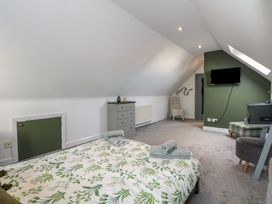 A bedroom with a bed covered in floral bedding a small green door a gray dresser a chair a wall-mounted TV and a skylight at Bryn-Y-Glyn in Penrhyn Bay
