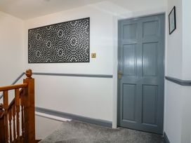 A hallway with a gray door a wooden staircase railing and a decorative black wall panel at Bryn-Y-Glyn in Penrhyn Bay