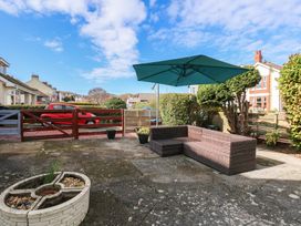 An outdoor patio area with a wicker corner sofa and a large green umbrella near a wooden gate with houses in the background at Bryn-Y-Glyn in Penrhyn Bay