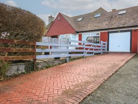 A house with a white garage door red brick walls a slanted roof and a paved driveway with a wooden fence at Bryn-Y-Glyn in Penrhyn Bay