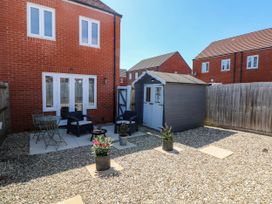 A backyard with gravel ground a small patio area with table chairs two armchairs a fire pit a shed and potted plants at Ty Bach Twt Llanelli