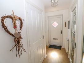 A hallway with a white front door a wooden floor a decorative heart hanging on the wall and a glass-paneled door at Ty Bach Twt Llanelli