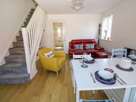 A living area with a white dining table set with plates and glasses a yellow armchair a red leather sofa stairs with grey carpet and a window at Ty Bach Twt Llanelli